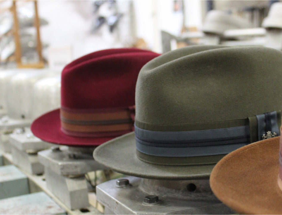 A red, green, and brown hats resting on hat blocks