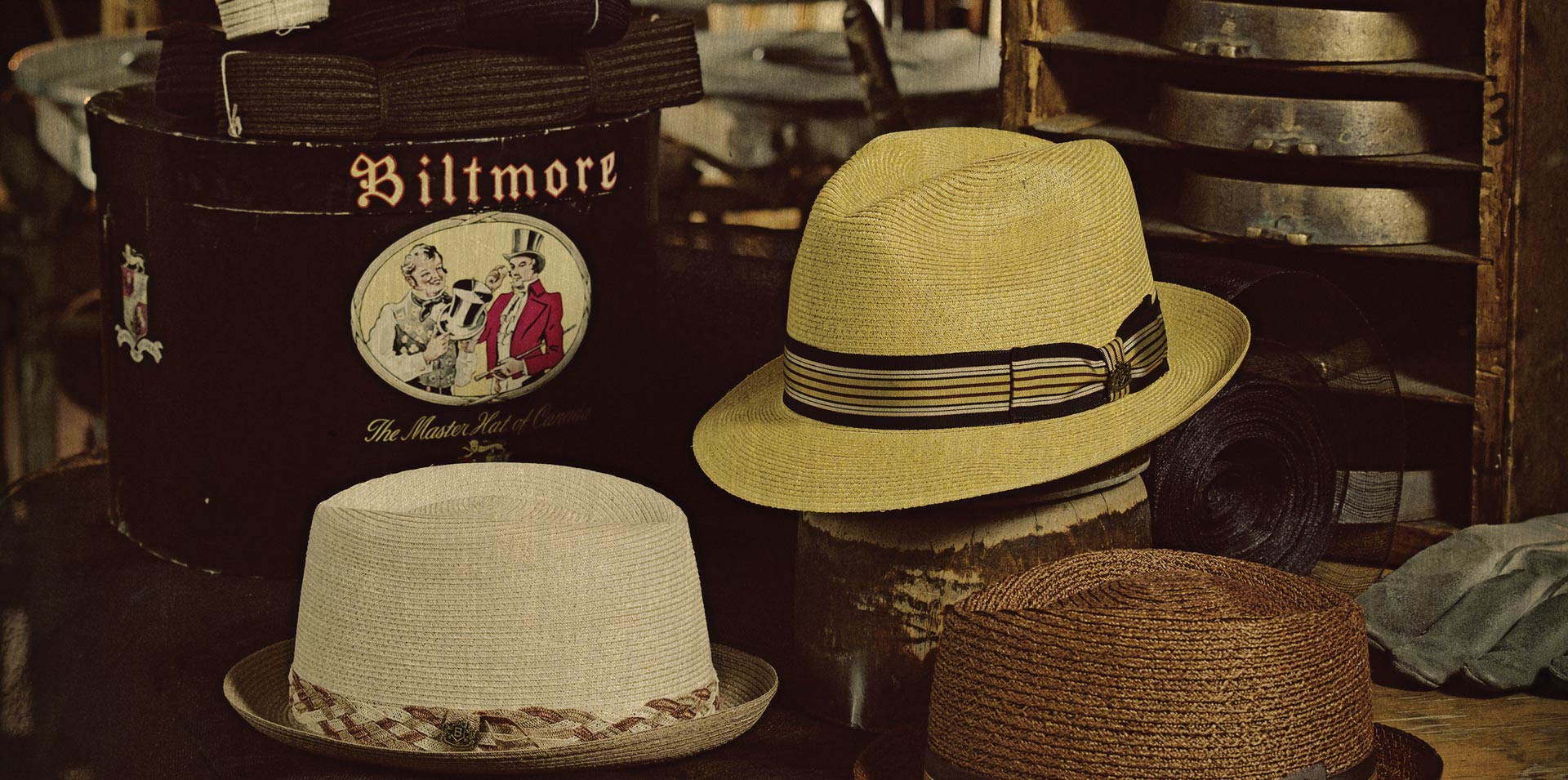 A sepia tone photo of hats resting on boxes branded with Biltmore near hat blocks on a shelf