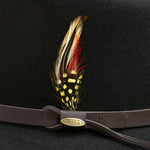 Feather decoration on a leather belt with gold Scala branding against a black hat