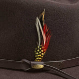 Chocolate colored hat with a decorative feather and leather band featuring a gold Scala brand logo
