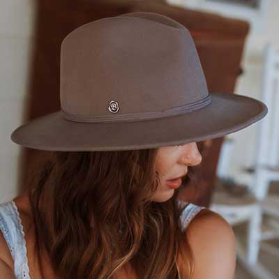Woman wearing a brown medium brimmed hat with a small shiny Biltmore pin attached on the side