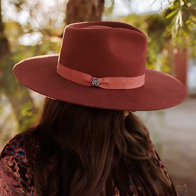 Woman wearing a red medium brimmed hat with red band and small shiny Biltmore pin attached on the side