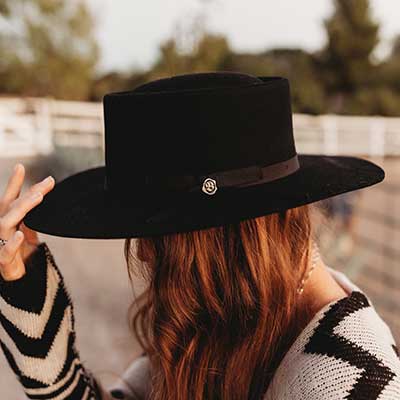 Woman wearing a black medium brimmed hat with a small shiny Biltmore pin attached to the side