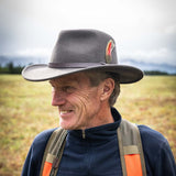 Smiling man wearing a gray fedora hat with a feather in a field