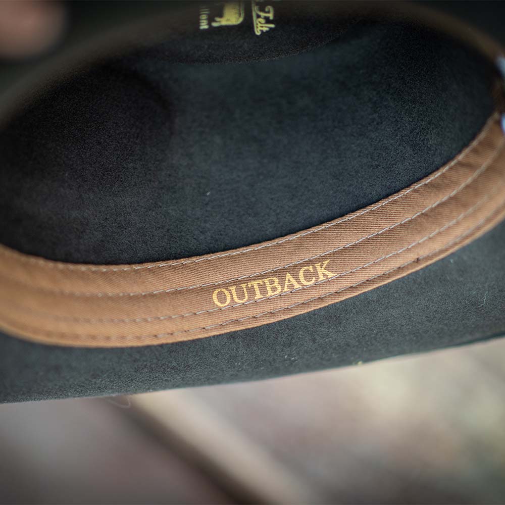 Chocolate colored fedora hat with a light brown band inside featuring 'OUTBACK' text on a blurred background