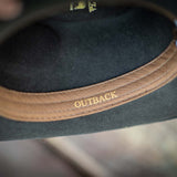 Chocolate colored fedora hat with a light brown band inside featuring 'OUTBACK' text on a blurred background