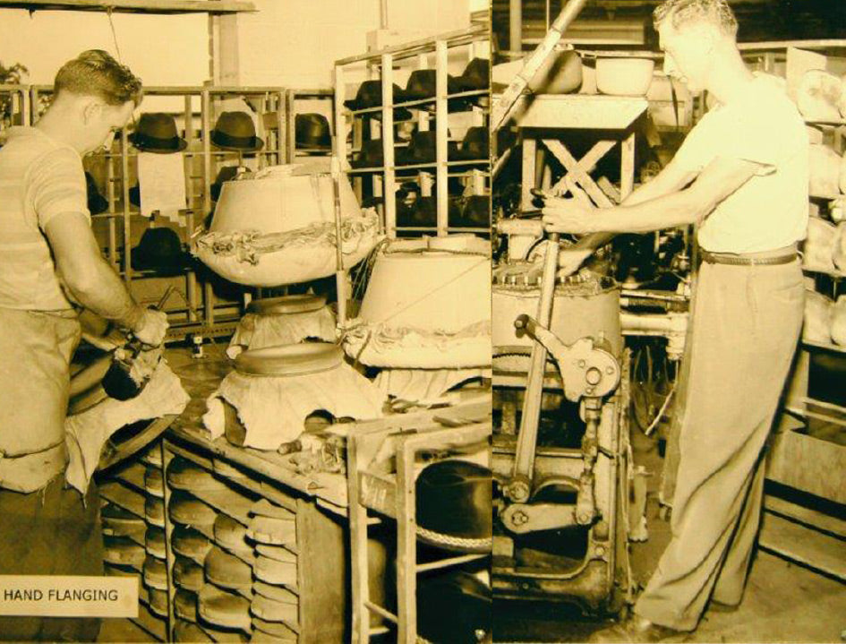 Old photograph of two men working on the fabric of hats next to a shelf full of dark colored hats