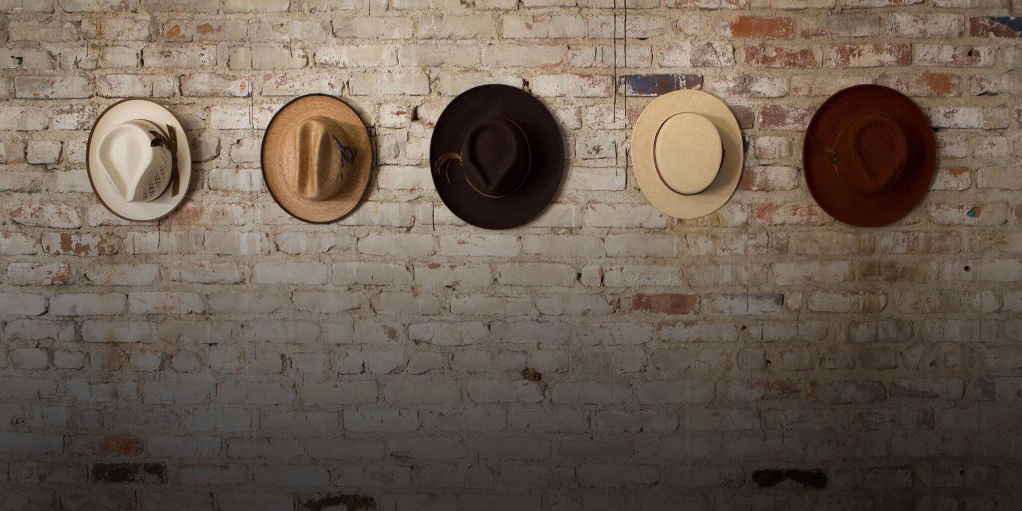 Multiple hats hooked up against a brick wall