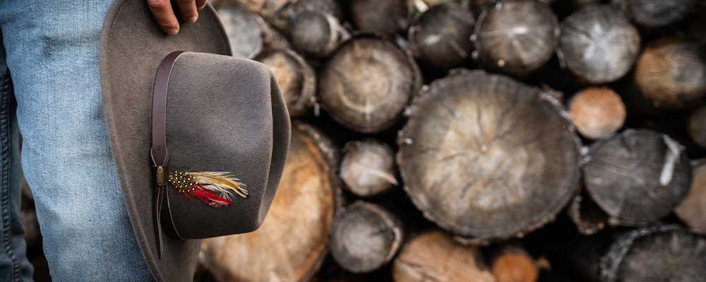 man holding Scala Dakota hat in front of log pile