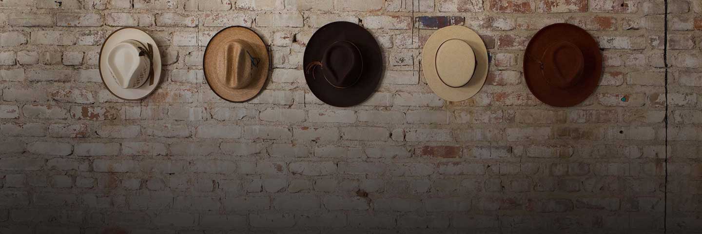 Five brown, tan, and white hats hanging on a brick wall