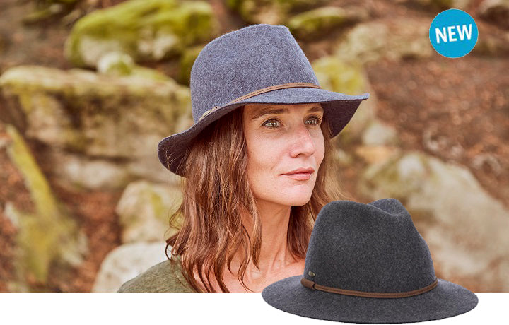 Woman wearing a gray hat looking upwards standing near a dirt and rocky area