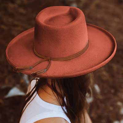 Woman wearing a auburn red medium brimmed hat with brown tassels wrapped around flared out at the back