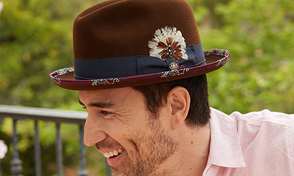 Smiling man wearing a brown hat with floral print and a pink shirt