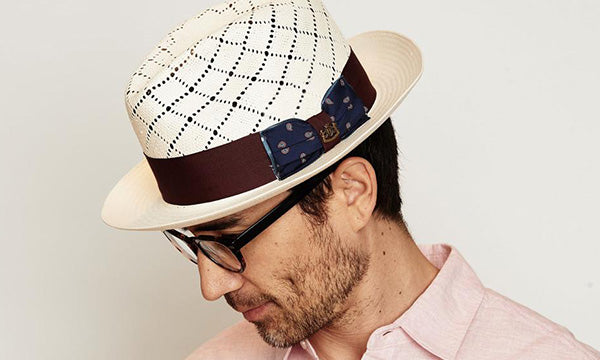 Man wearing a white hat with black perforated stripes and brown band and a pink shirt