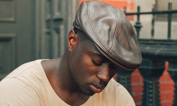 Man wearing a brown hat and tan shirt looking towards the ground with his eyes shut