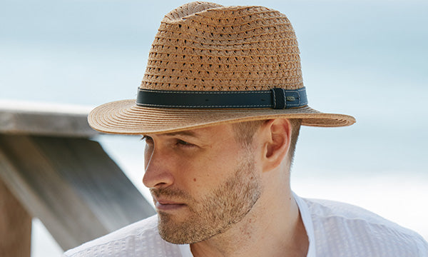 Man wearing a brown hat with black band with air holes near a beach