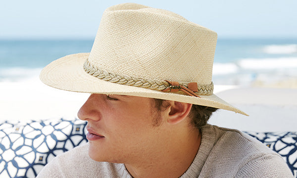 Man wearing a light tan hat sitting on a blue and white floral couch near the ocean