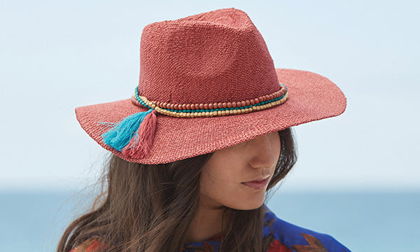 Woman wearing a red hat with multi-colored rope for a band standing near the ocean